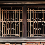 An intricately carved wooden window lattice from an ancient Chinese courtyard house, featuring delicate plum blossom and bamboo patterns, under soft, natural lighting. Adjacent to the window, a weathered brick wall showcases subtle relief carvings of auspicious bats. The scene emphasizes rich textures of aged wood and brick, conveying historical craftsmanship. Professional photography, highly detailed, realistic, high resolution, safe for work, appropriate content, fully clothed, modest, family-friendly.